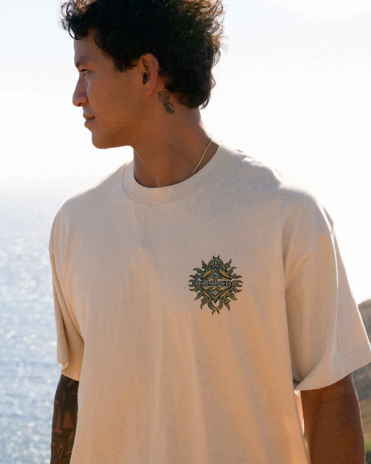 Oatmeal-colored t-shirt with small black graphic print on chest featuring a sun design with decorative elements.