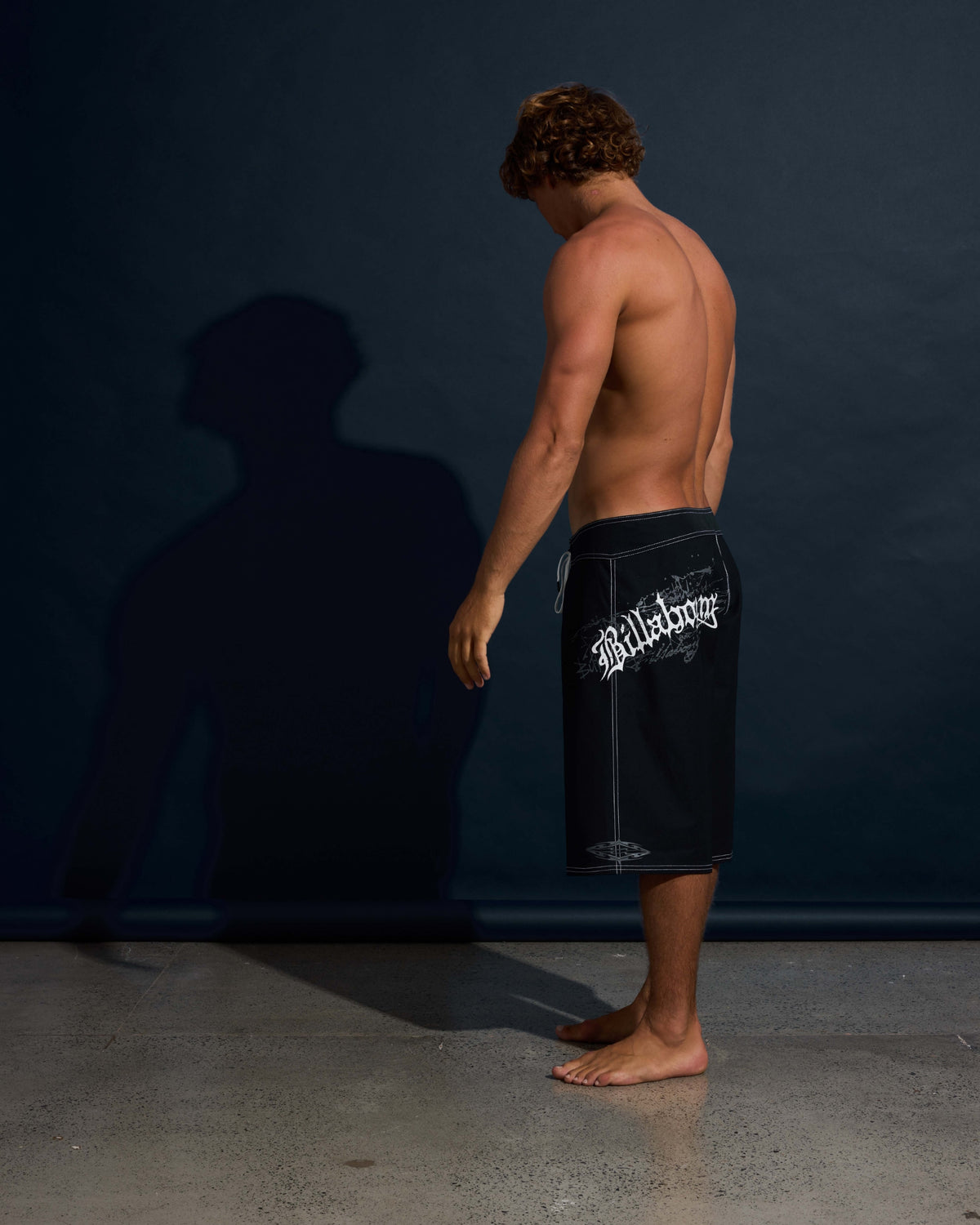 Black boardshorts with white graphic text and drawstring waist, knee-length fit.