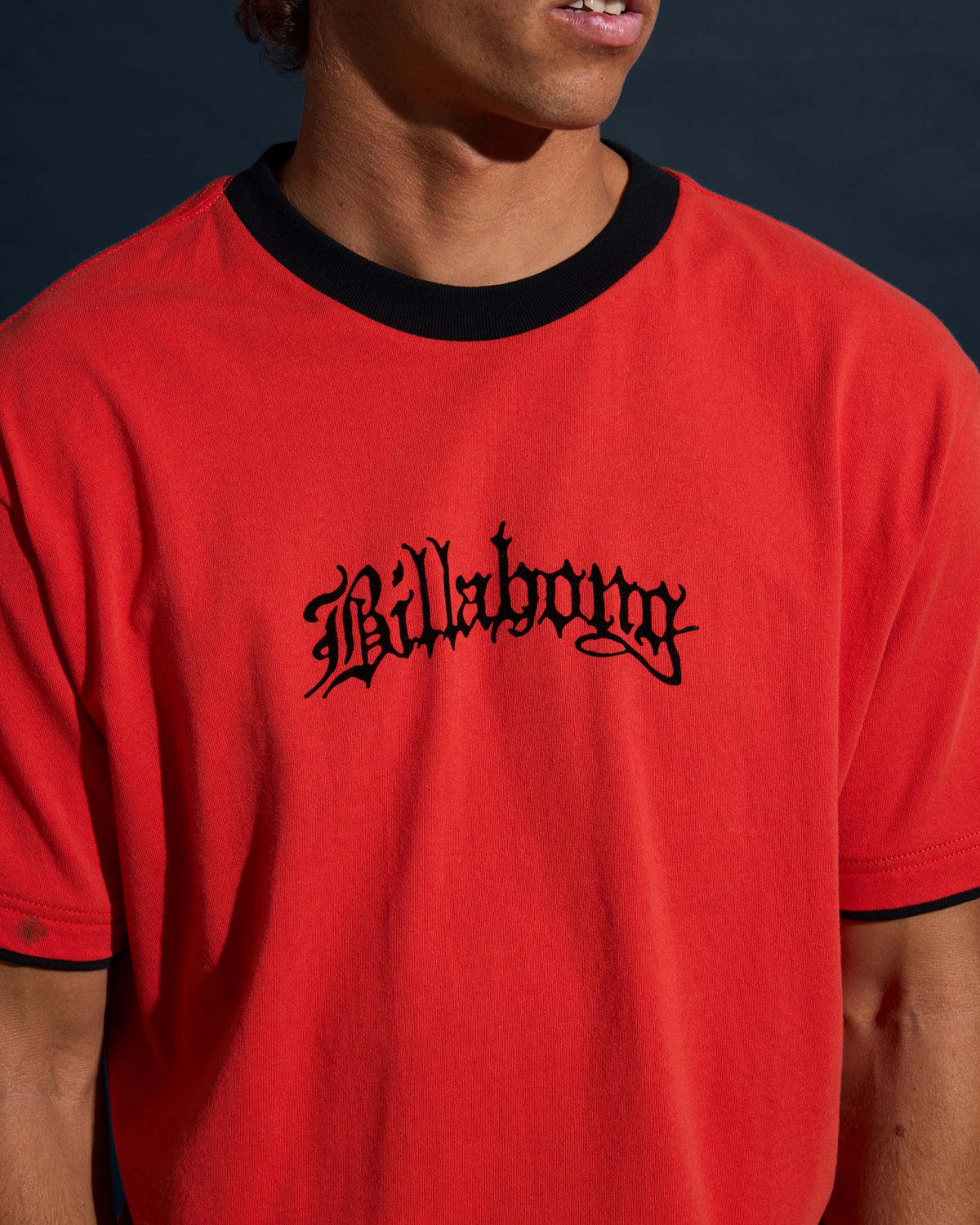 Deep red short sleeve t-shirt with black crew neckline and "Billabong" text graphic on chest.