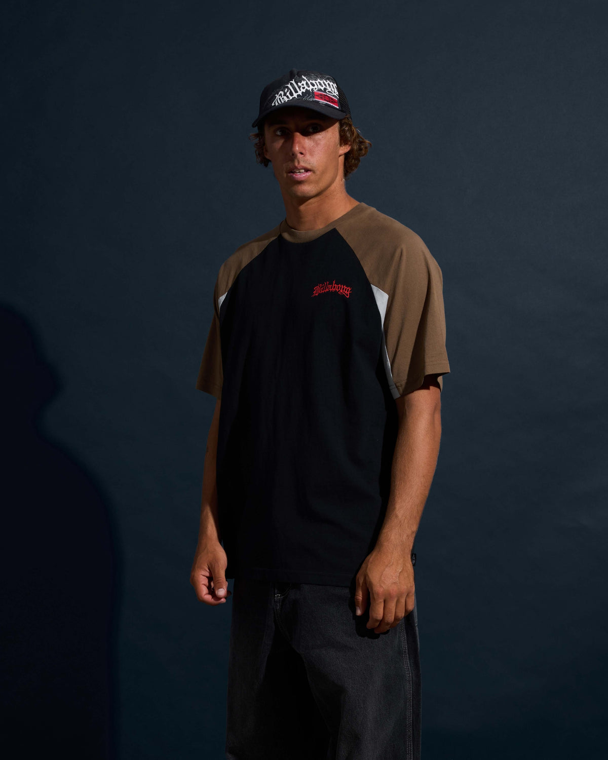 Black short-sleeve t-shirt with tan raglan sleeves and red text logo on chest.