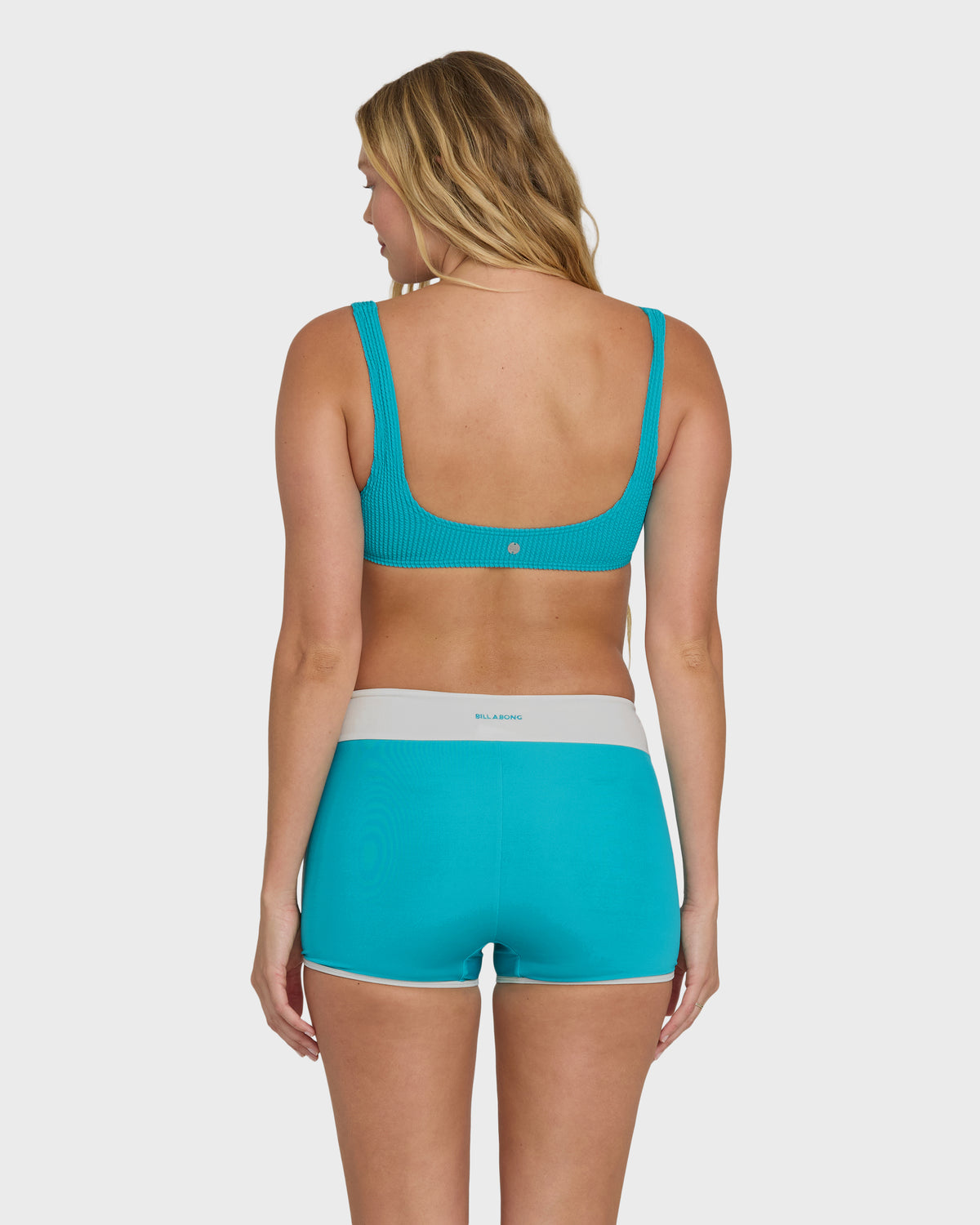Woman wearing bright marine boardshorts with white waistband and matching ribbed bikini top, back view.