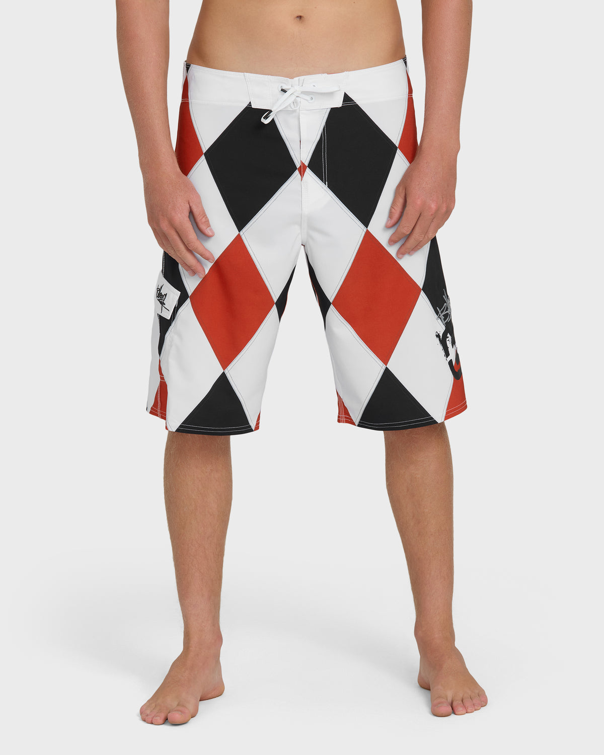 Men's boardshorts with red, black, and white diamond pattern, white drawstring, knee-length cut.
