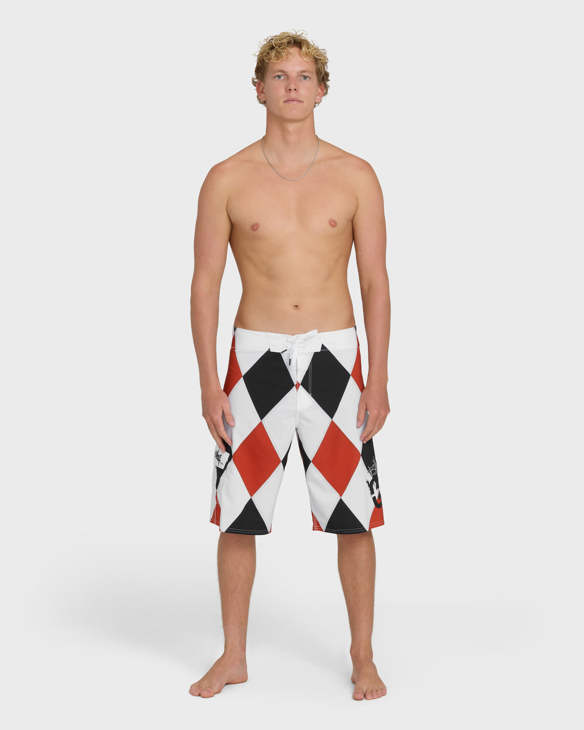 Red, white, and black diamond-patterned boardshorts with drawstring waist, worn by male model.