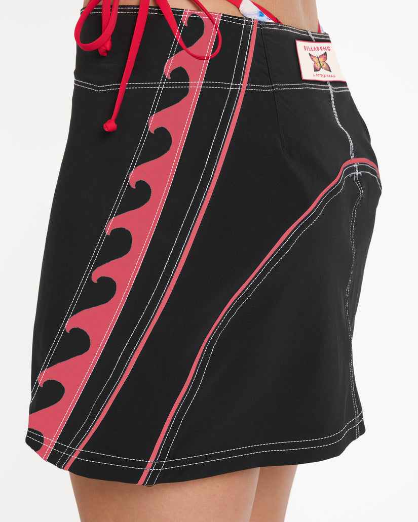 Off-black boardshort skirt with pink contrast panels, scalloped details, white stitching, and pink drawstring waist.