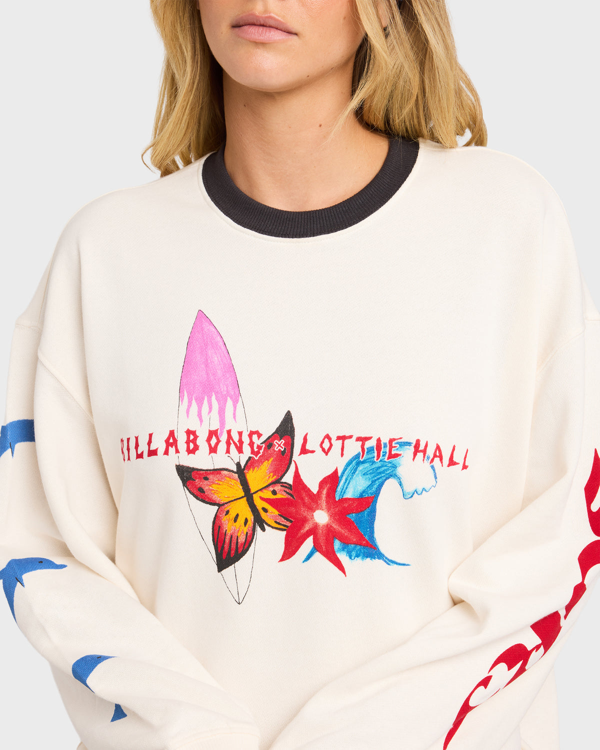 Cream crewneck sweatshirt with black ribbed neckline and multicolored graphic print featuring surfboards, butterfly, and flow