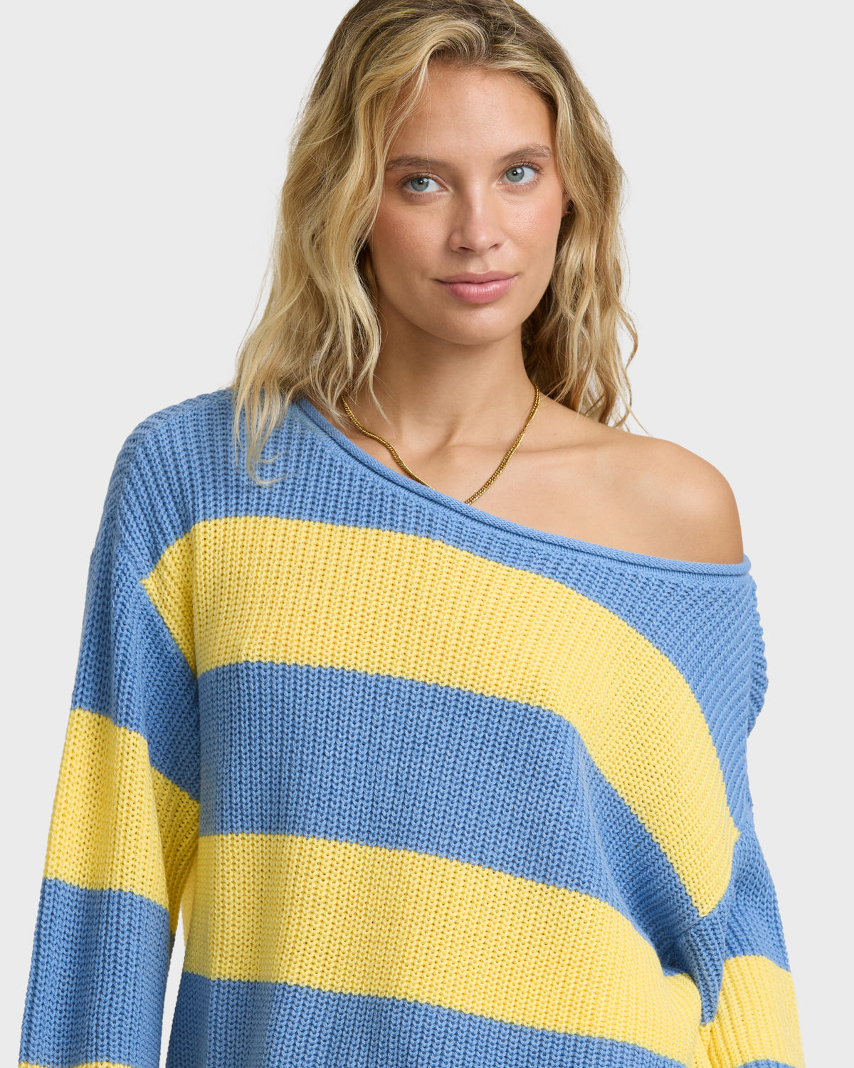 Woman wearing off-shoulder blue and yellow striped knit sweater with long sleeves.