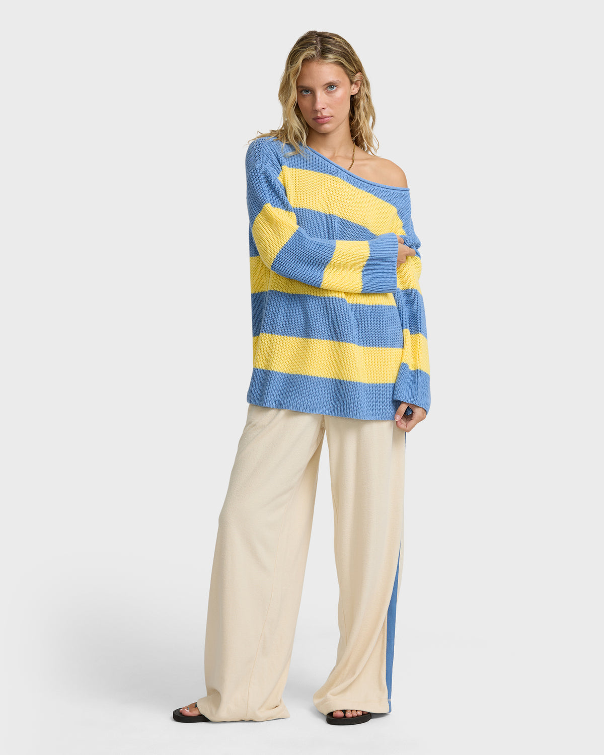 Blue and yellow striped off-shoulder ribbed sweater worn with cream pants.
