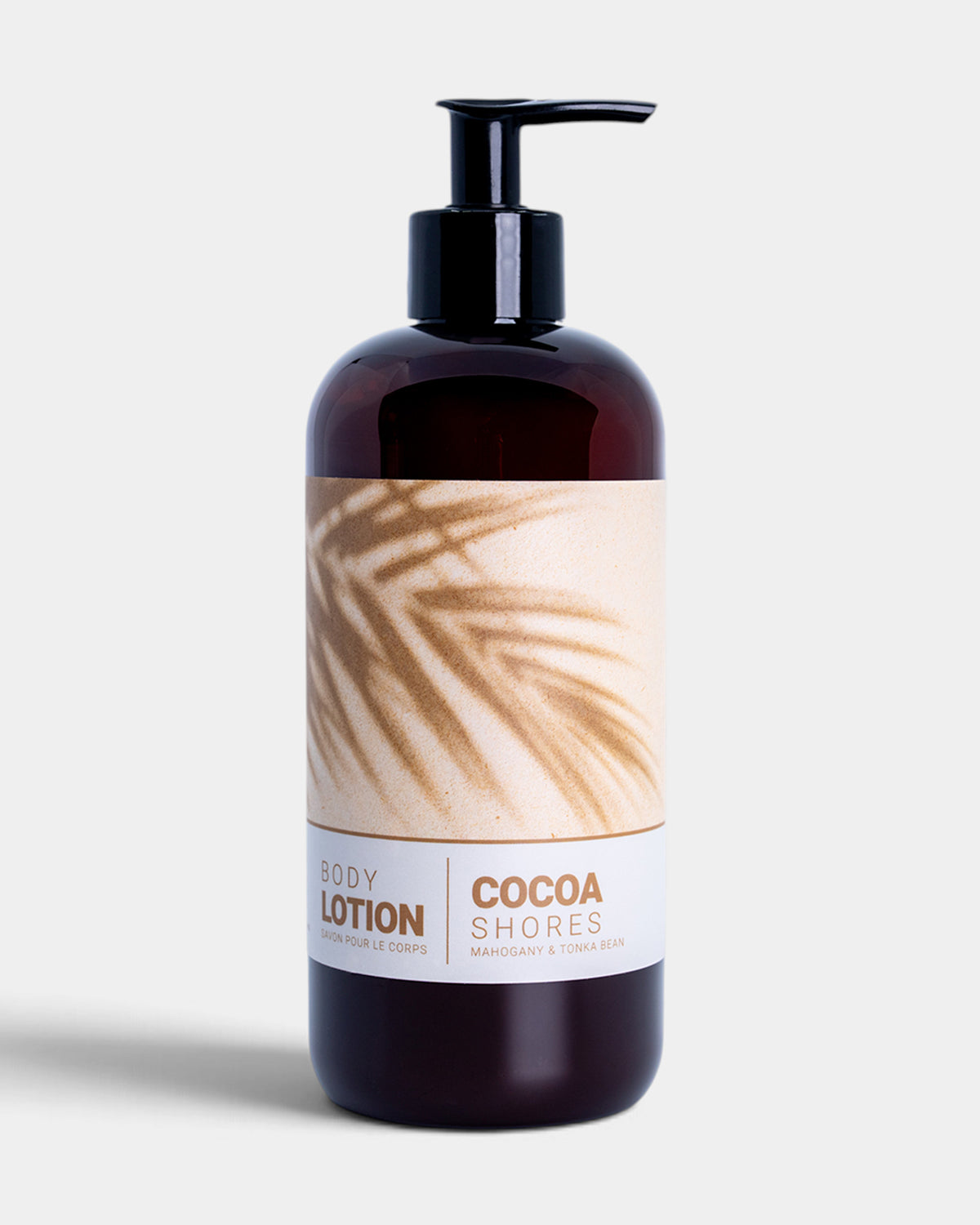 A dark amber bottle of Cocoa Shores Body Lotion with a black pump dispenser and a beige label featuring a palm leaf pattern, set against a light gray background.