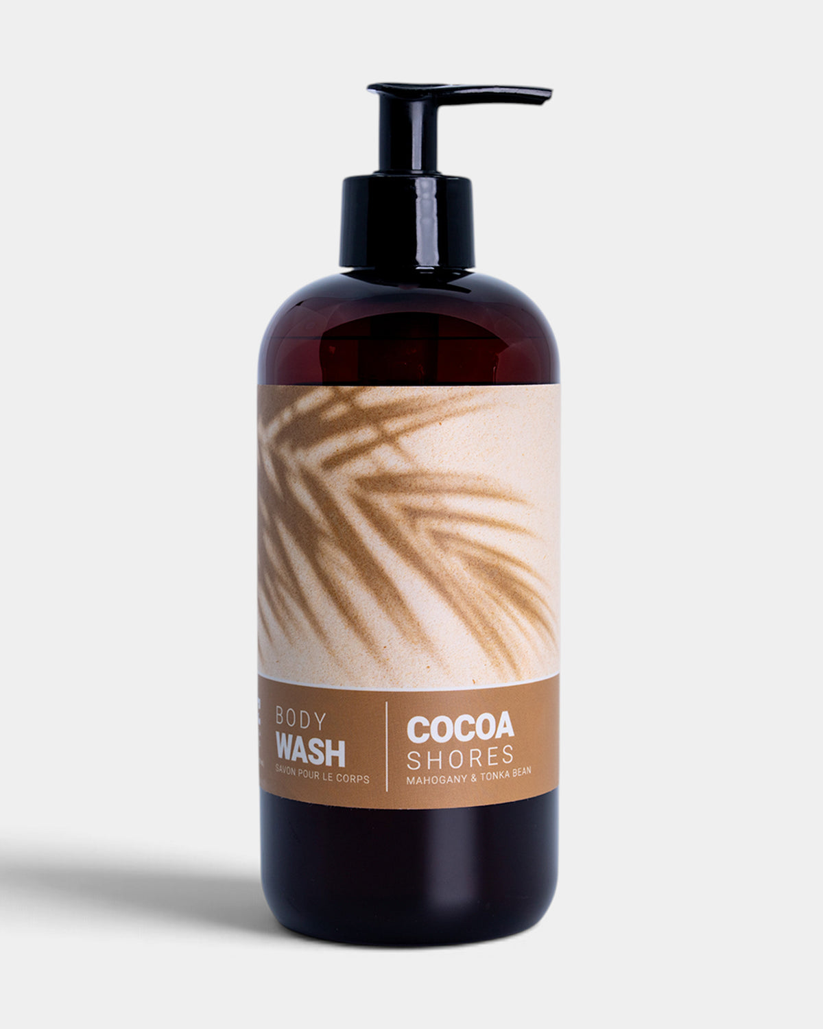 A dark amber bottle of Cocoa Shores body wash with a black pump dispenser and a beige label featuring a palm leaf pattern, set against a light gray background.