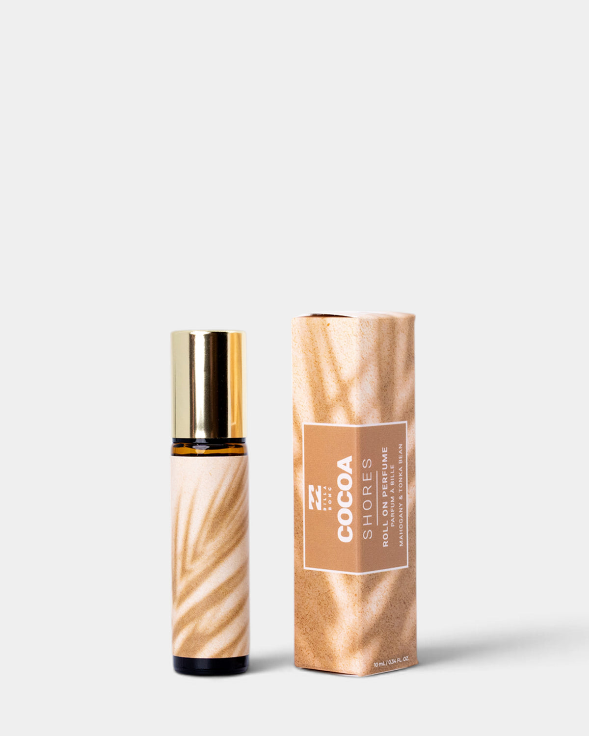 A small amber glass roller bottle with a gold cap stands beside its matching cylindrical box. Both pieces feature a warm tan and brown leaf-patterned wrap and a central white label reading 'COCOA SHORES' and 'ROLL ON PERFUMES'.