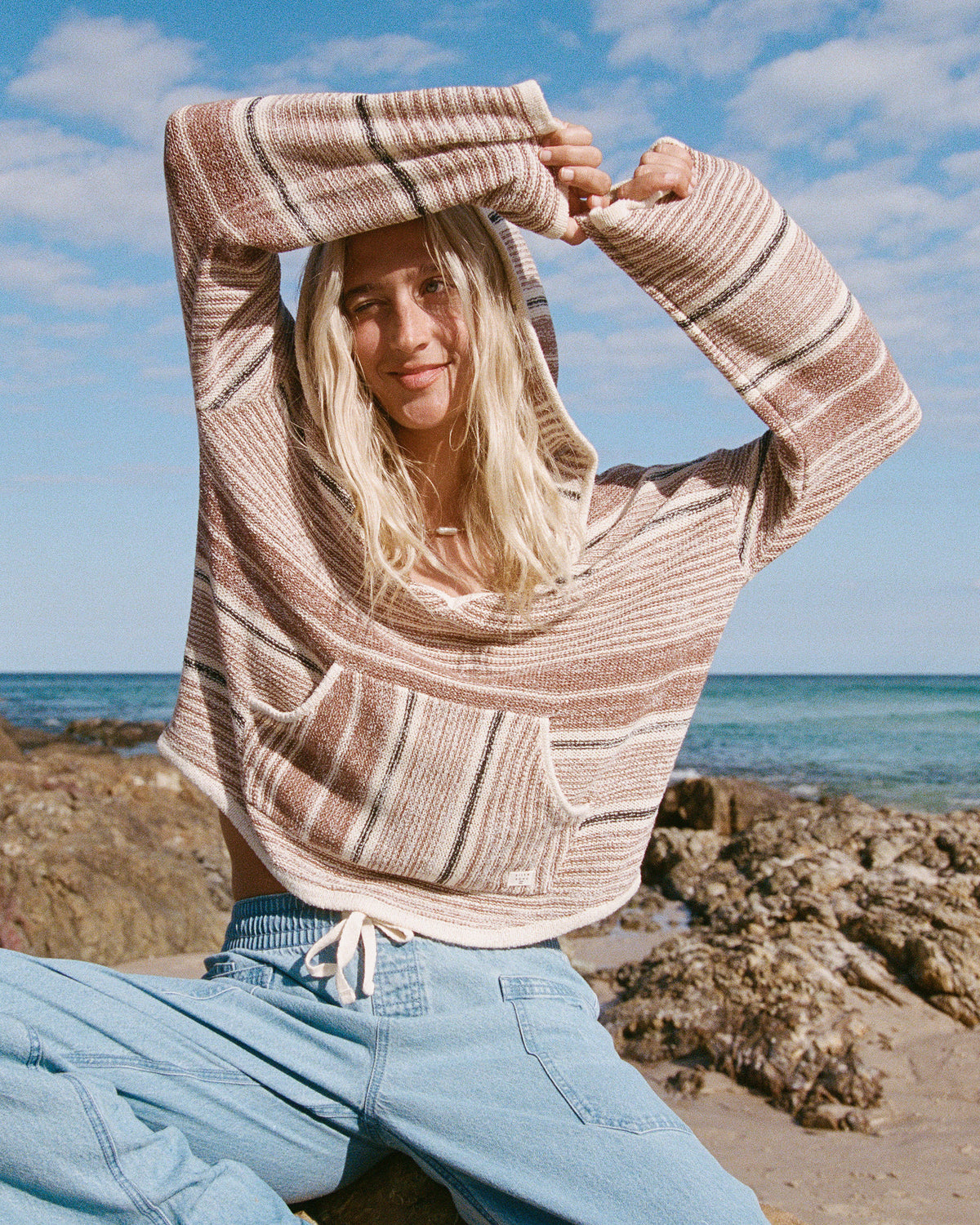 Striped hooded sweater in white and brown with ribbed texture and front pocket, worn with light blue jeans.