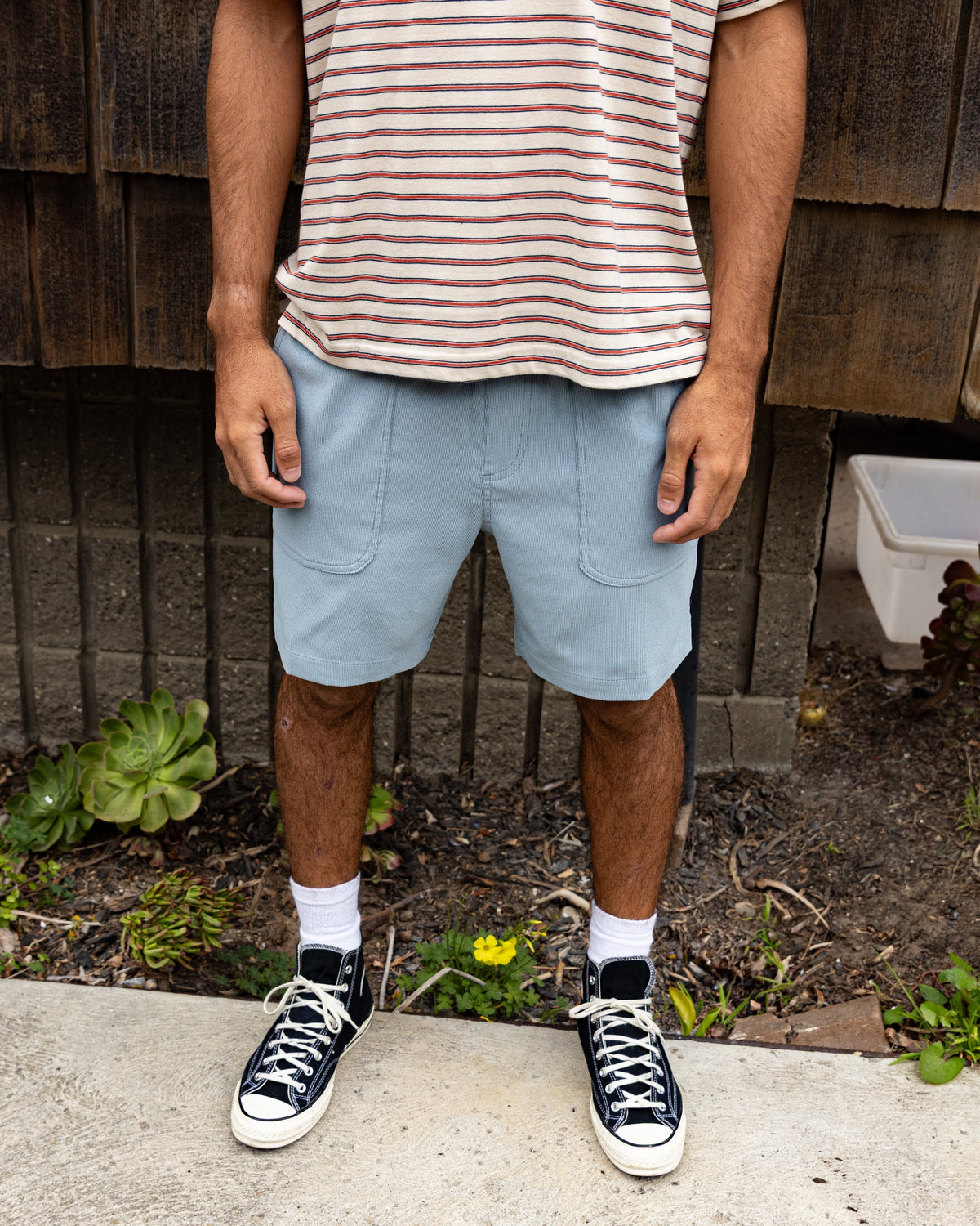 Light blue hybrid shorts with front patch pockets, worn with striped shirt and black canvas sneakers.