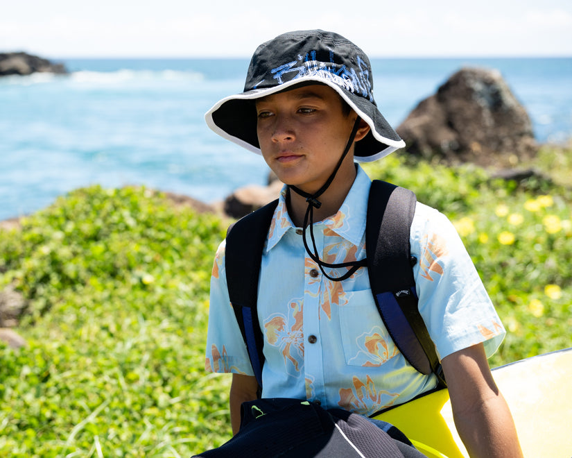 Person wearing a bucket hat and carrying a backpack by the ocean