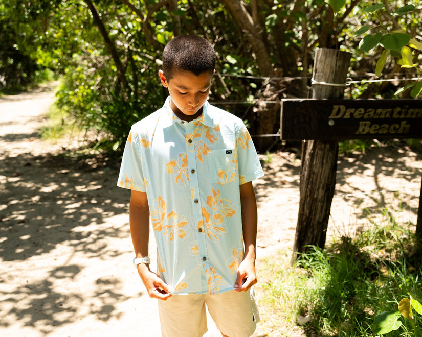 Person wearing a light blue floral shirt standing near a wooden signpost in a natural setting.