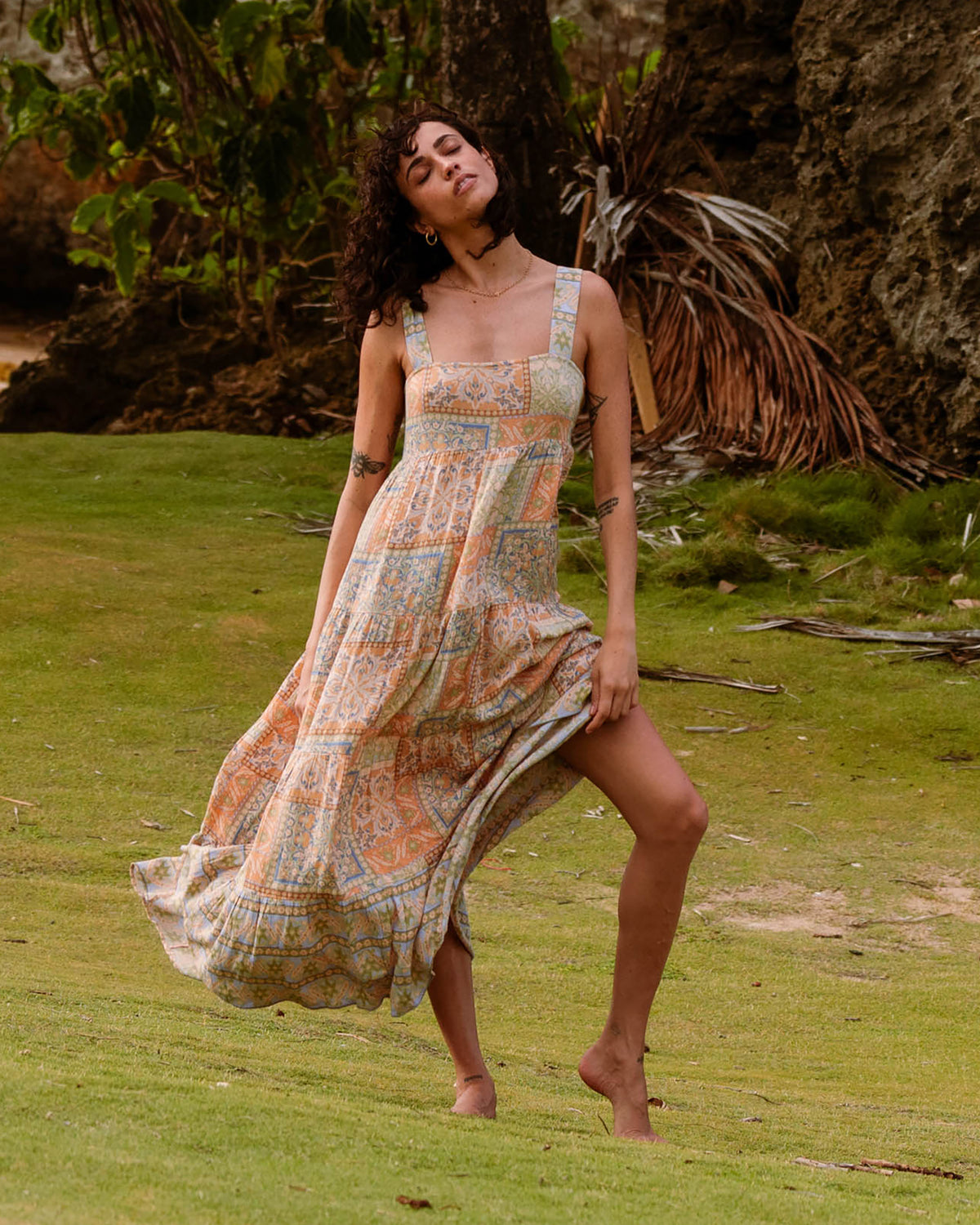 Woman wearing a sleeveless maxi dress with multicolored paisley print and square neckline, flowing to ankles.
