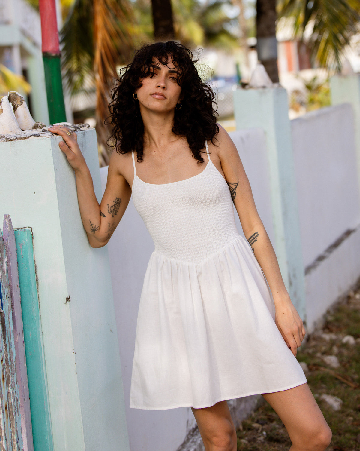 White sleeveless mini dress with ribbed bodice and flowing skirt on model against painted wall.