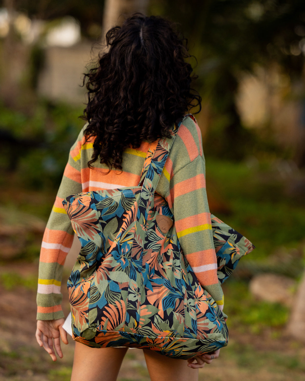 Black multi-colored tote bag with floral print, worn on shoulder by person outdoors.
