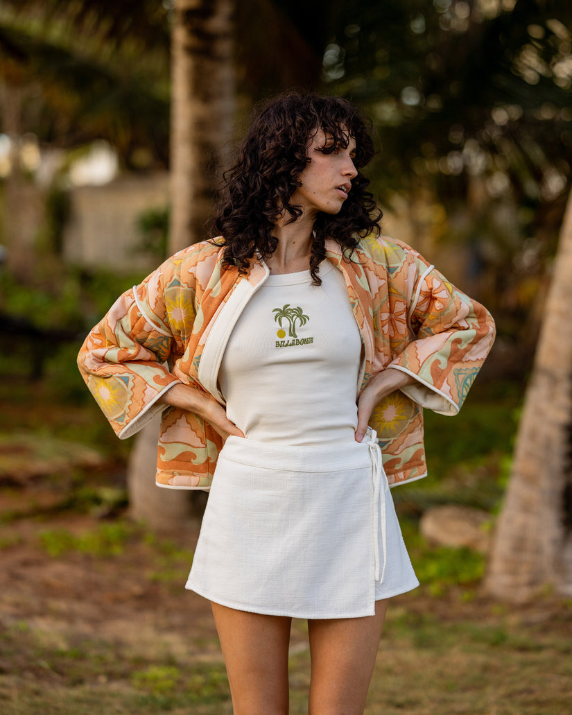 Sand-colored quilted jacket with floral pattern, worn open over white top.