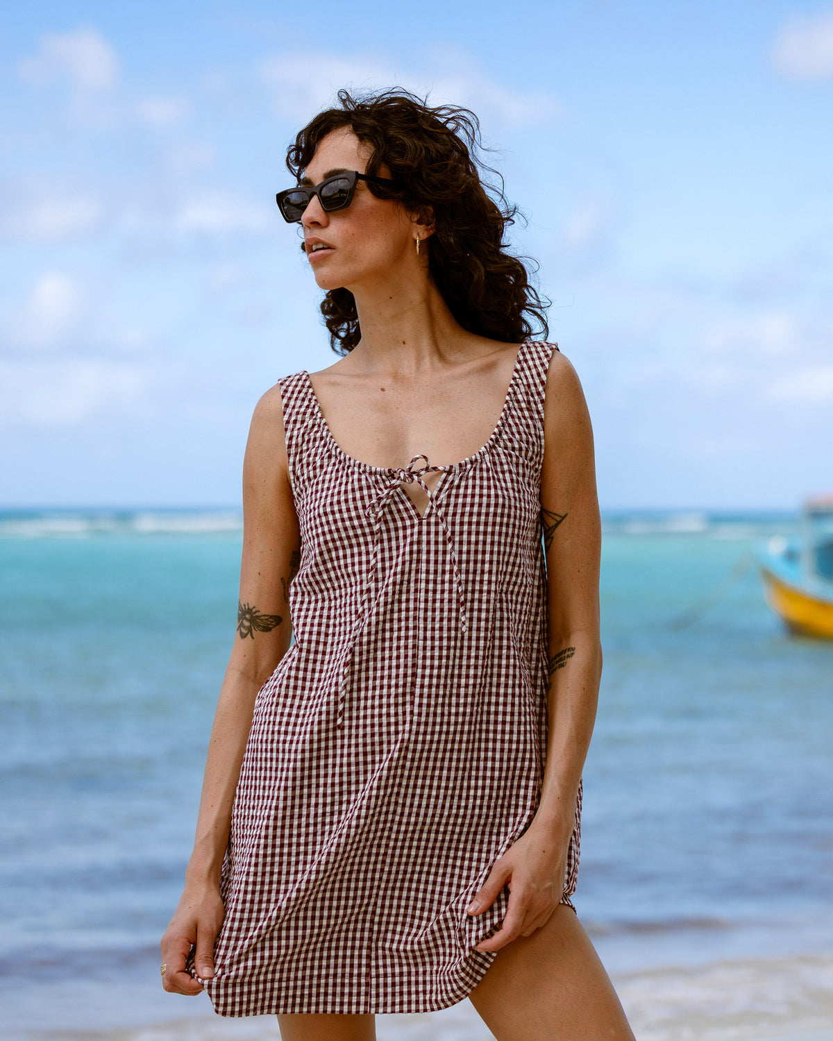 Red and white gingham sleeveless dress with front tie detail on a woman at the beach.