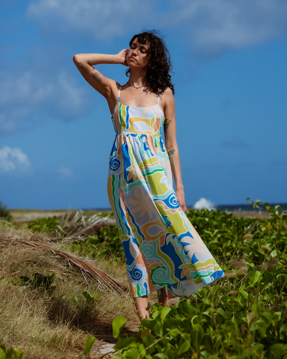 Blue, yellow, and green multi-colored midi dress with abstract pattern and thin straps worn by woman outdoors.