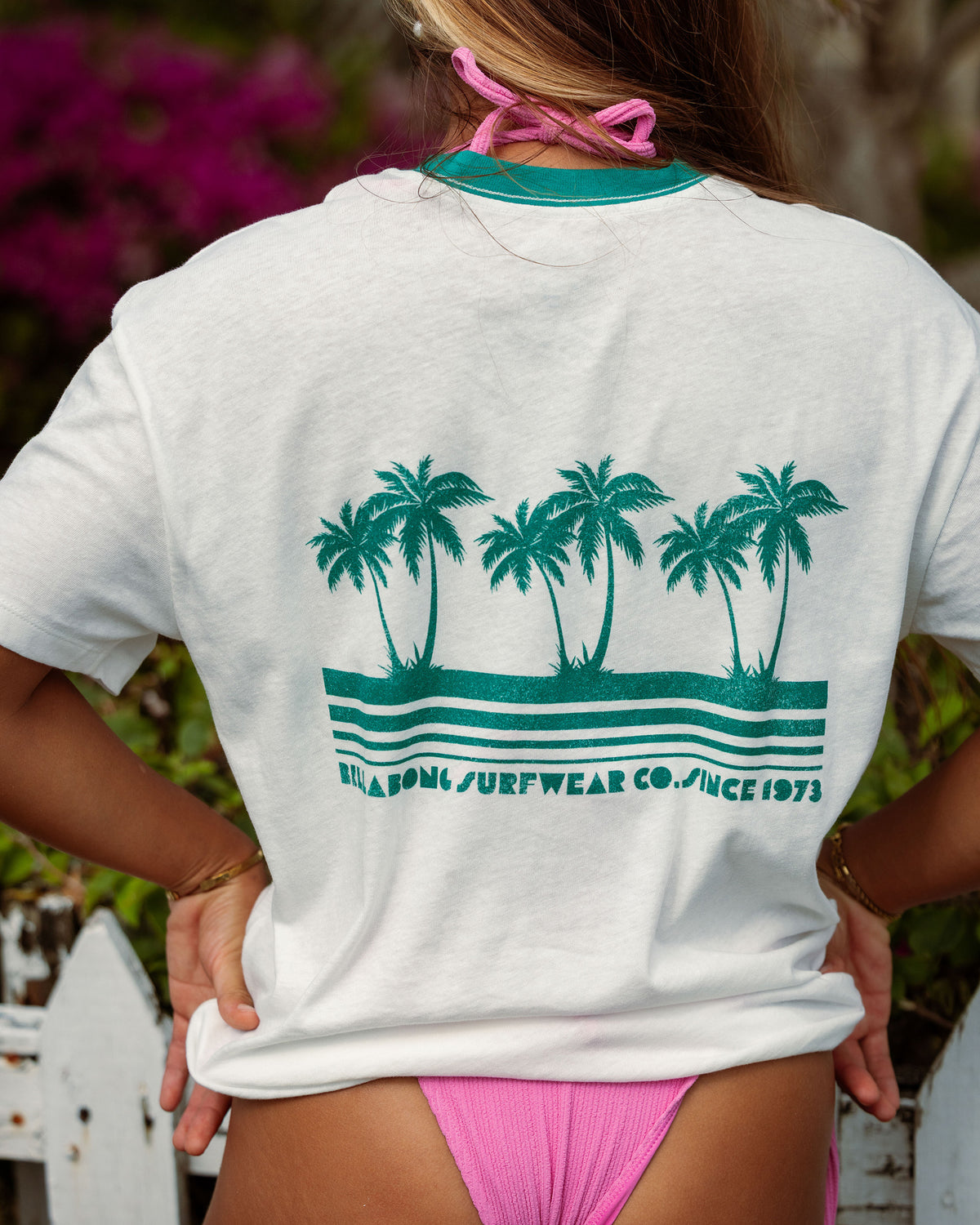 White short-sleeve t-shirt with teal palm tree and wave graphic on back, teal crew neckline.