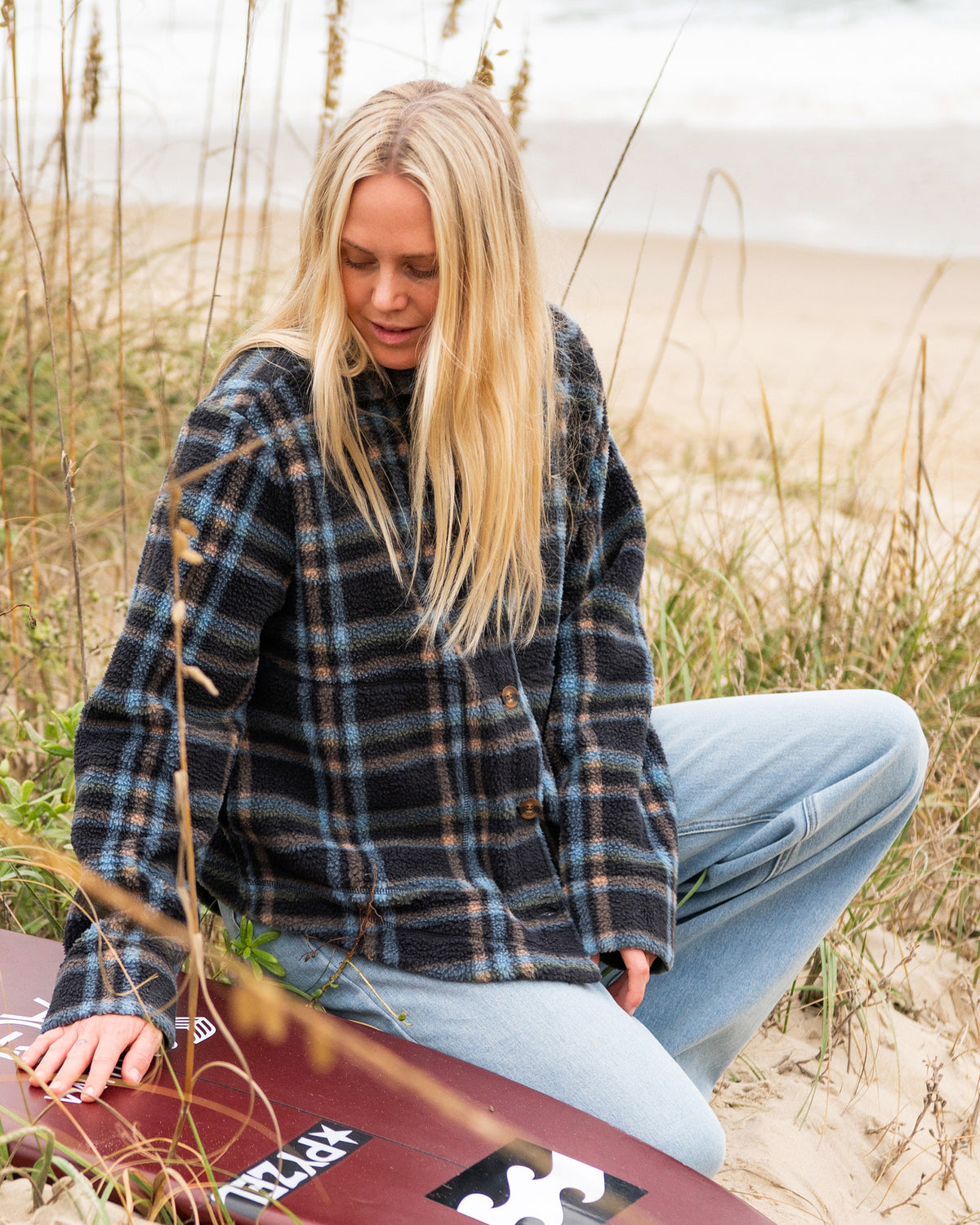 Woman wearing black plaid sherpa shacket with button front, paired with light blue jeans on a beach.