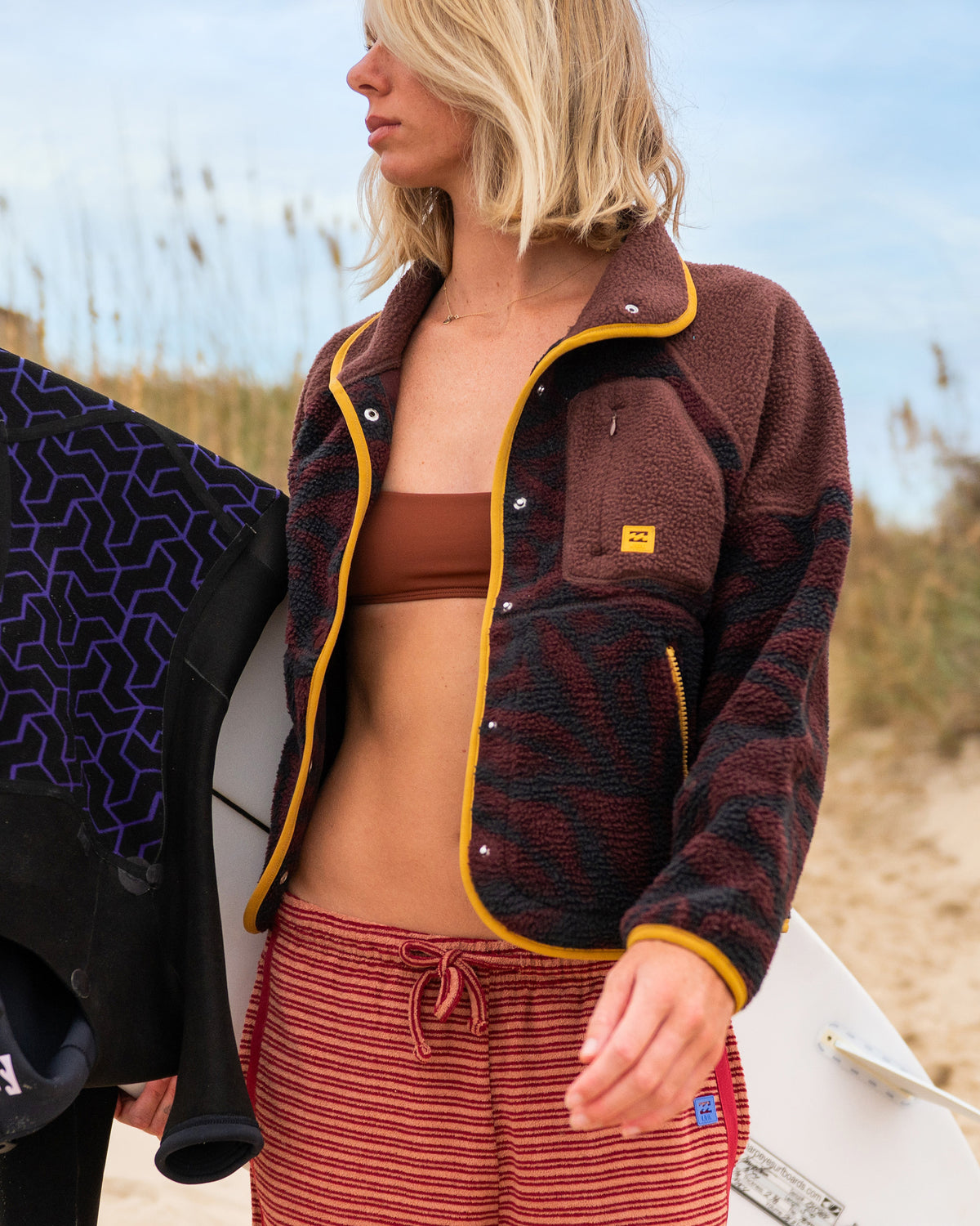 Teak sherpa fleece jacket with mustard yellow trim and snap closures worn over a brown bikini top.