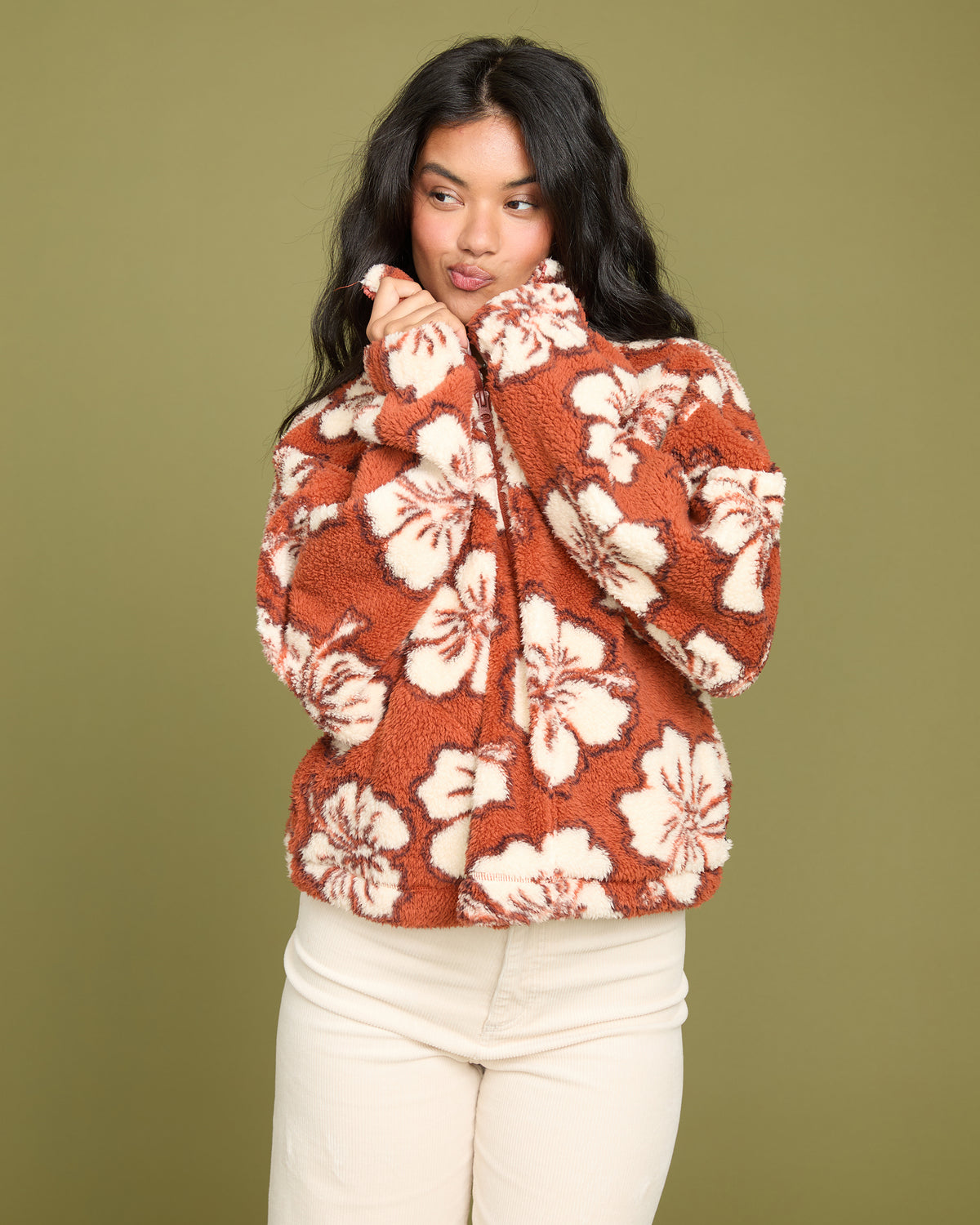 Rust-colored sherpa half zip sweatshirt with cream floral pattern, worn with cream pants.
