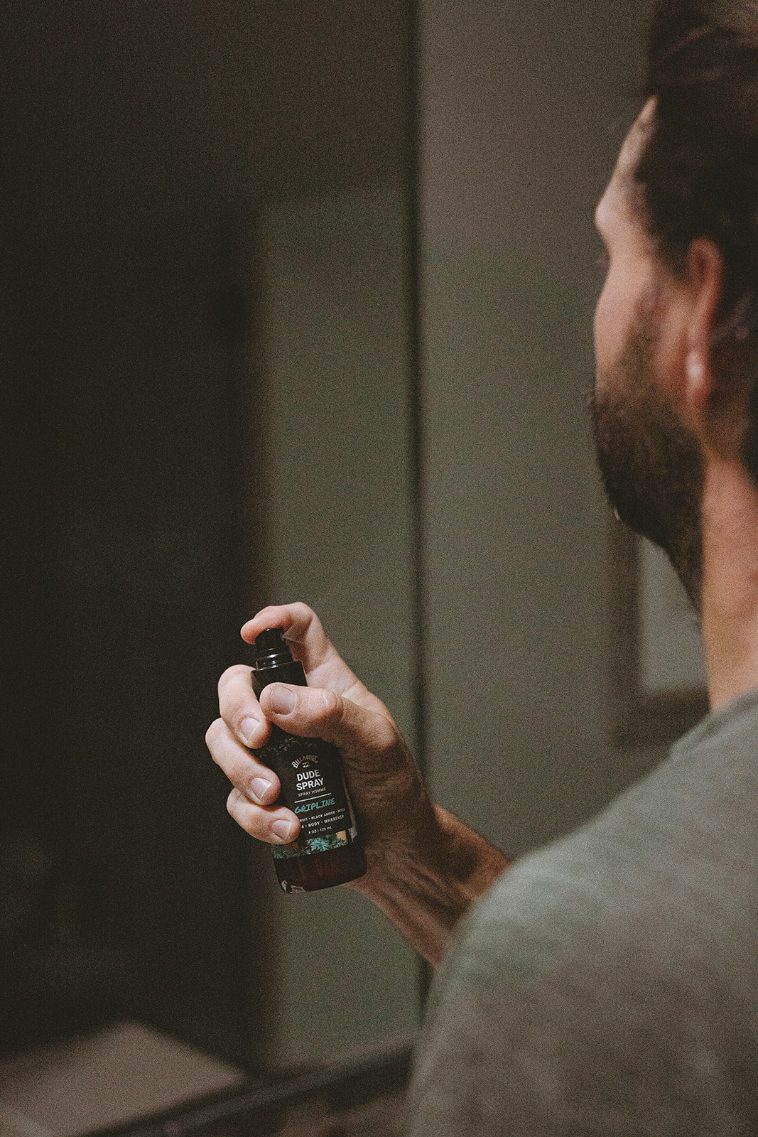 Man holding black spray bottle labeled "Dude Spray" with dark background.