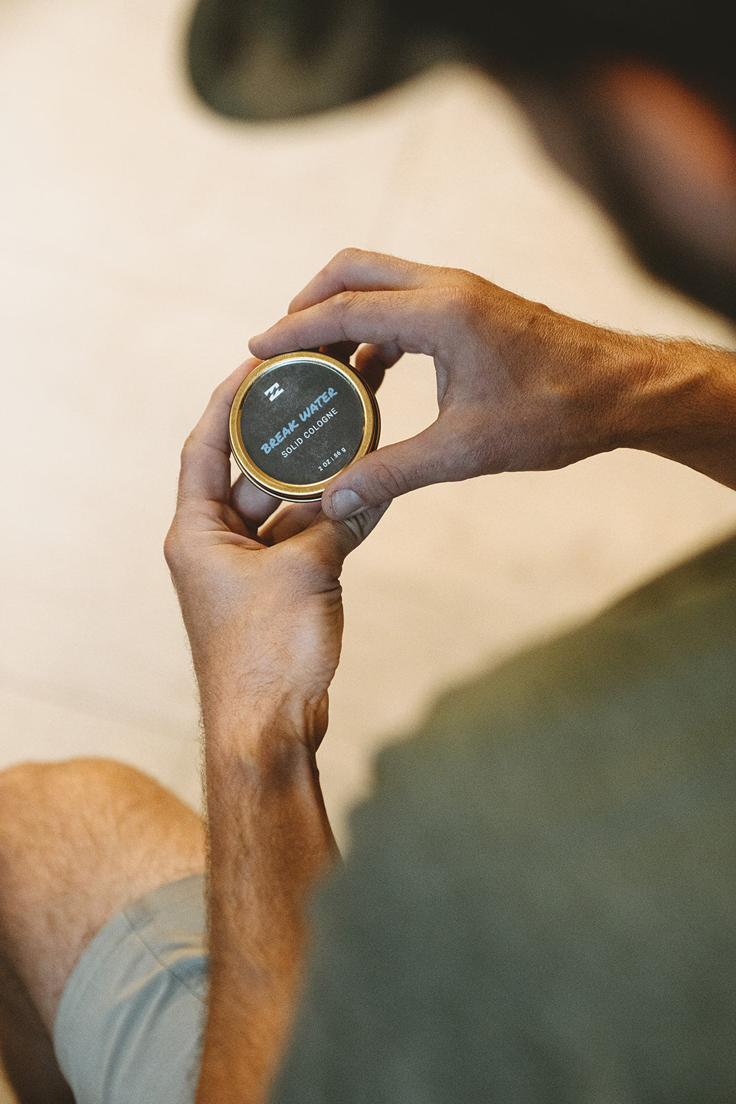 Round solid cologne tin with black label and gold rim held in person's hands.