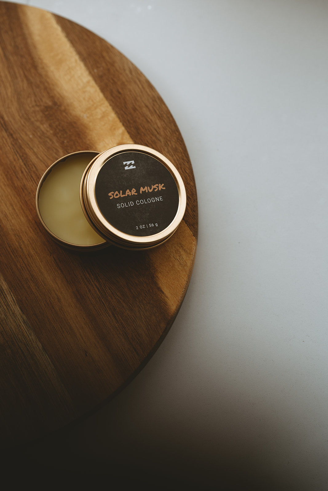 Open tin of Solar Musk solid cologne with pale yellow product inside, 2 oz, displayed on wooden surface.