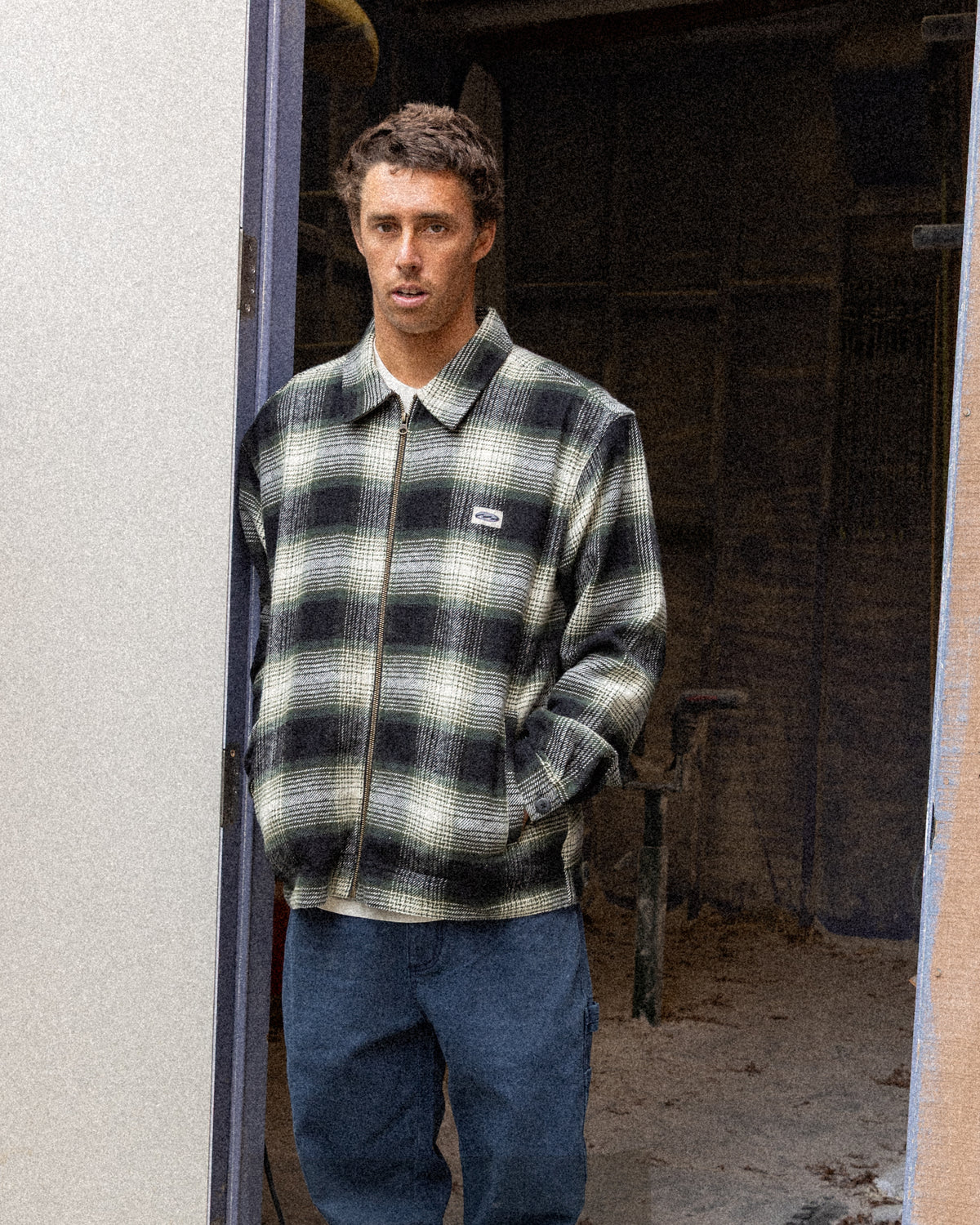 Man wearing black and white plaid zip-up jacket with collar over blue jeans.