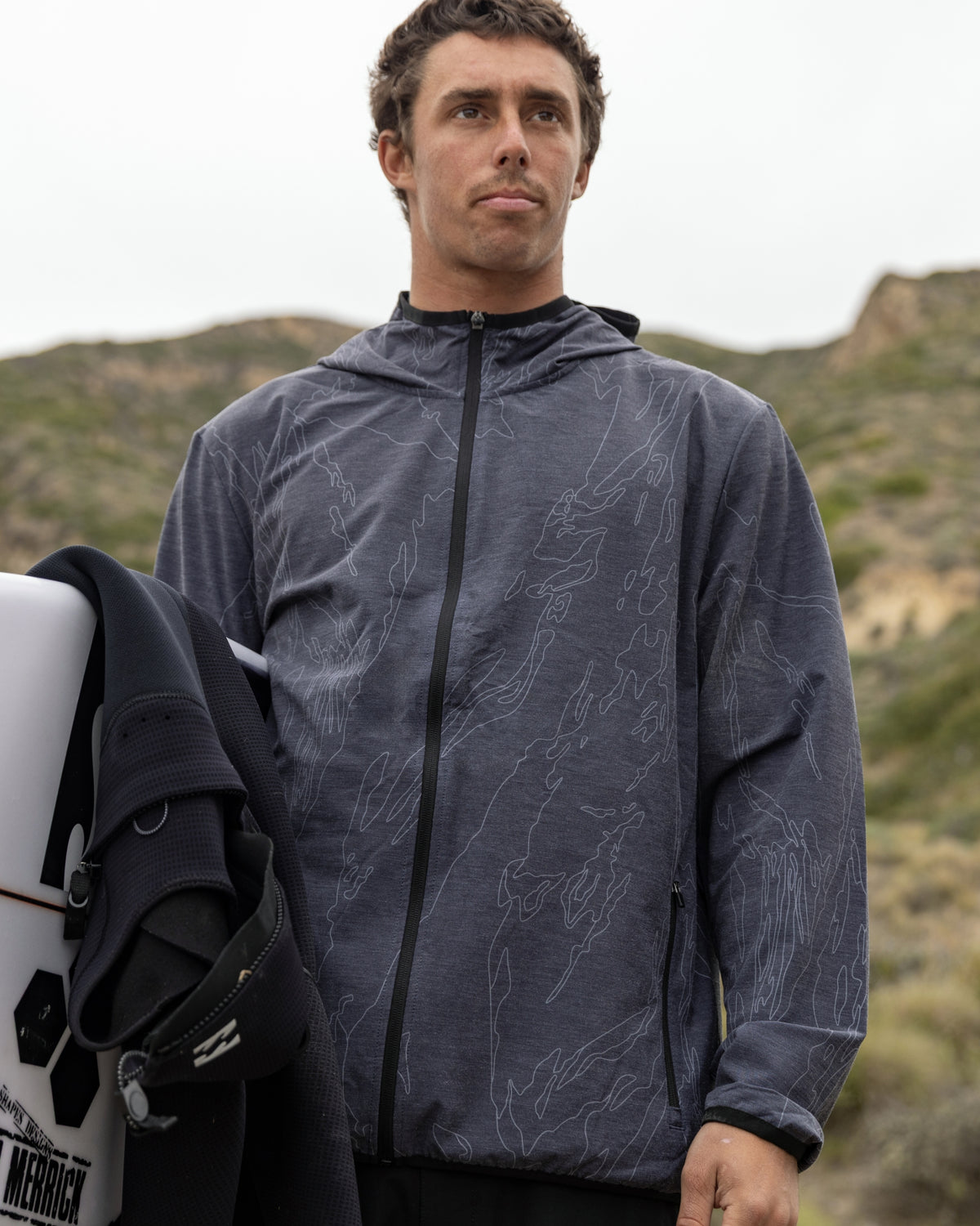 Man wearing black camo stretch shell jacket with hood and full-length zip over mountainous terrain.