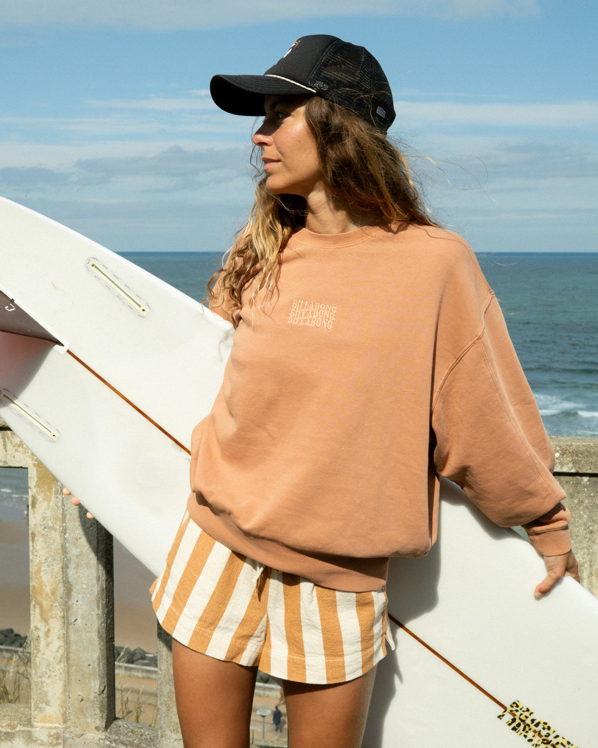 Caramel-colored crewneck sweatshirt with embroidered text on chest, worn with striped shorts.