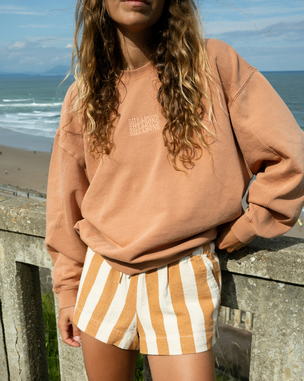 Caramel-colored crewneck sweatshirt with small text logo on chest.